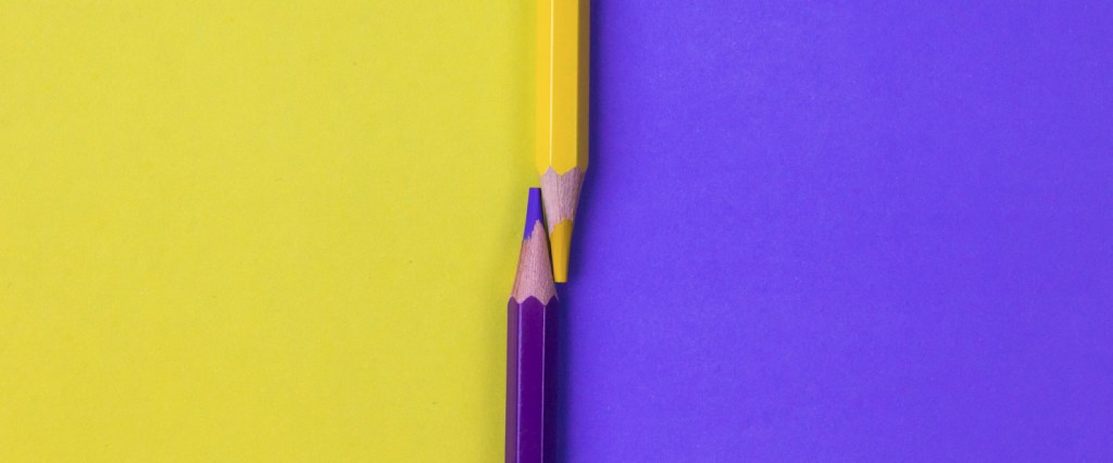 Curso de finanças: conheça 15 opções gratuitas para aprender. Ilustração de dois lápis conectados pelas pontas formando uma linha vertical no centro da imagem, cuja cor é preenchida metade em amarelo e a outra em roxo.