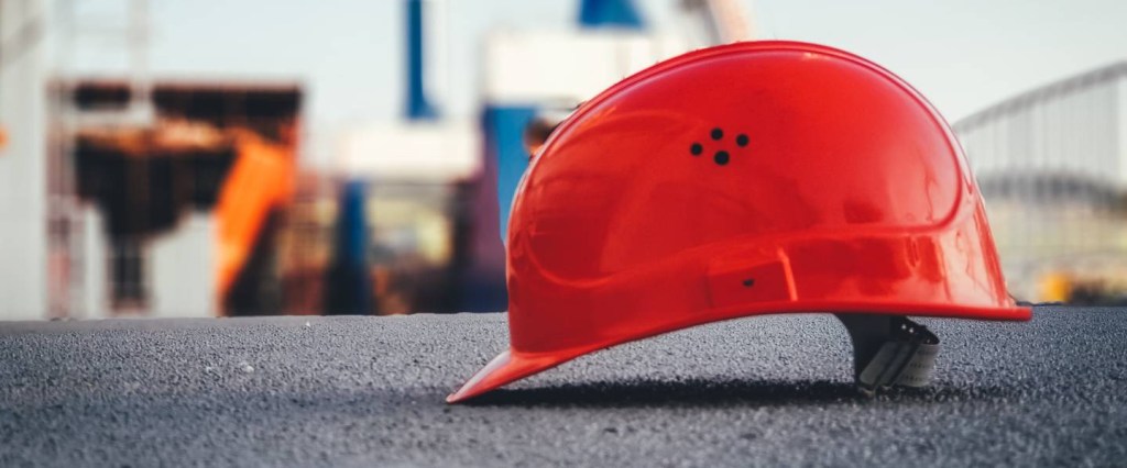 Imagem mostra um capacete de obra vermelho sobre uma superfície de concreto.
