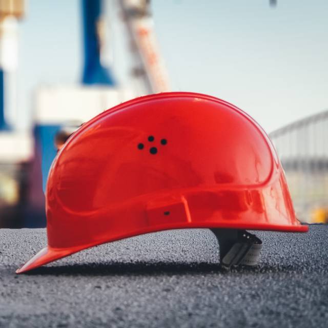 Imagem mostra um capacete de obra vermelho sobre uma superfície de concreto.
