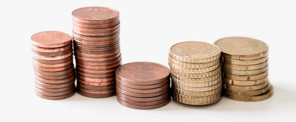 Imagem mostra três s pilhas de moedas sobre um fundo branco.