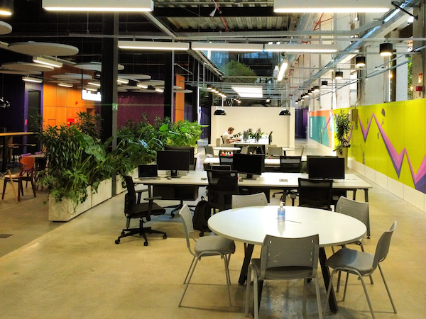 Imagem do escritório do Nubank na Vila Leopoldina, em São Paulo. Mesas e cadeiras dispostas em um ambiente colorido