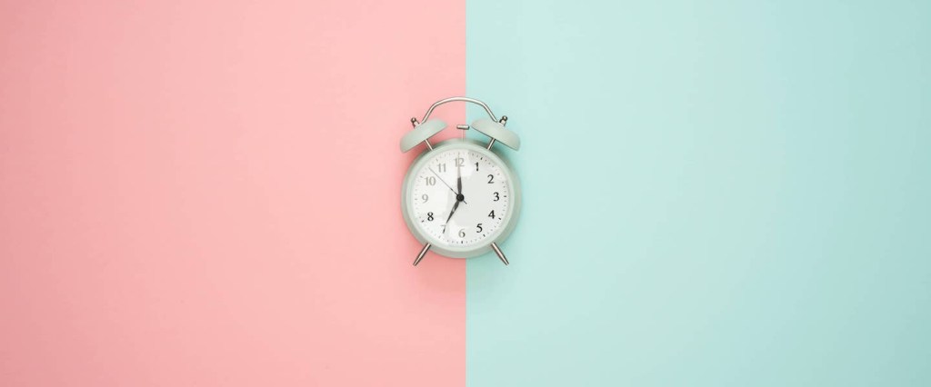 Foto de um relógio no centro de duas cores: uma rosa e outra azul claro. Foto por Icons8