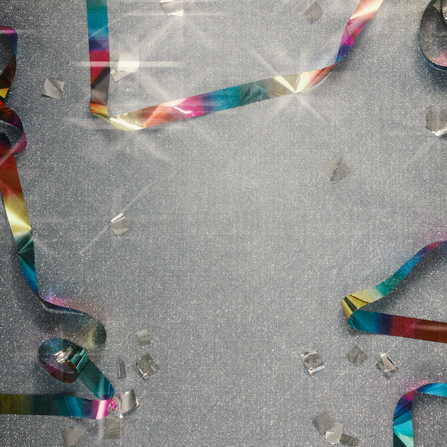 Imagem de confete e serpentinas coloridas e brilhantes numa superfície cinza.