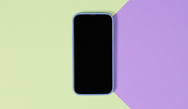 Imagem de um celular desligado sobre um fundo metade lilás, metade verde claro.