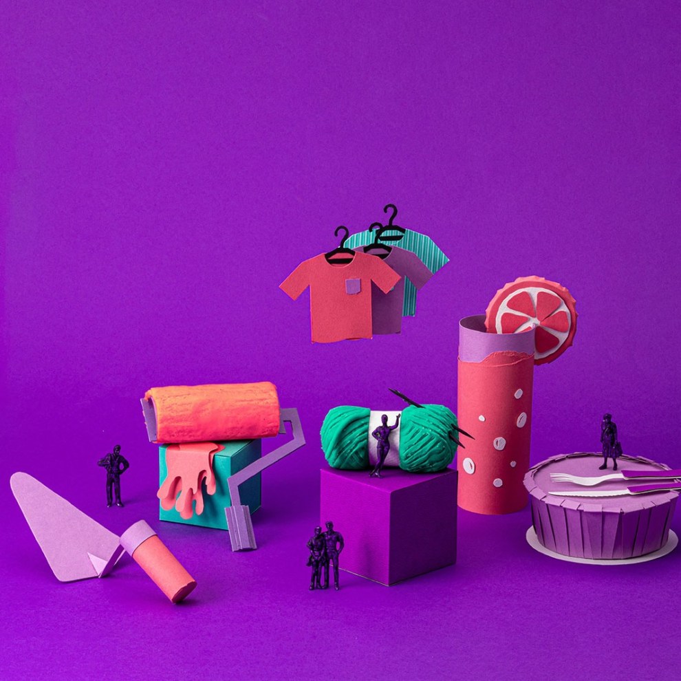 Na imagem aparecem diversos objetos de toy art sobre um fundo roxo. Pode-se ver itens relacionados à construção, como uma pá, um drink, uma marmita, duas peças de roupa, um rolo de tinta. Todos são de cores vibrantes em tons de roxo, verde e rosa.