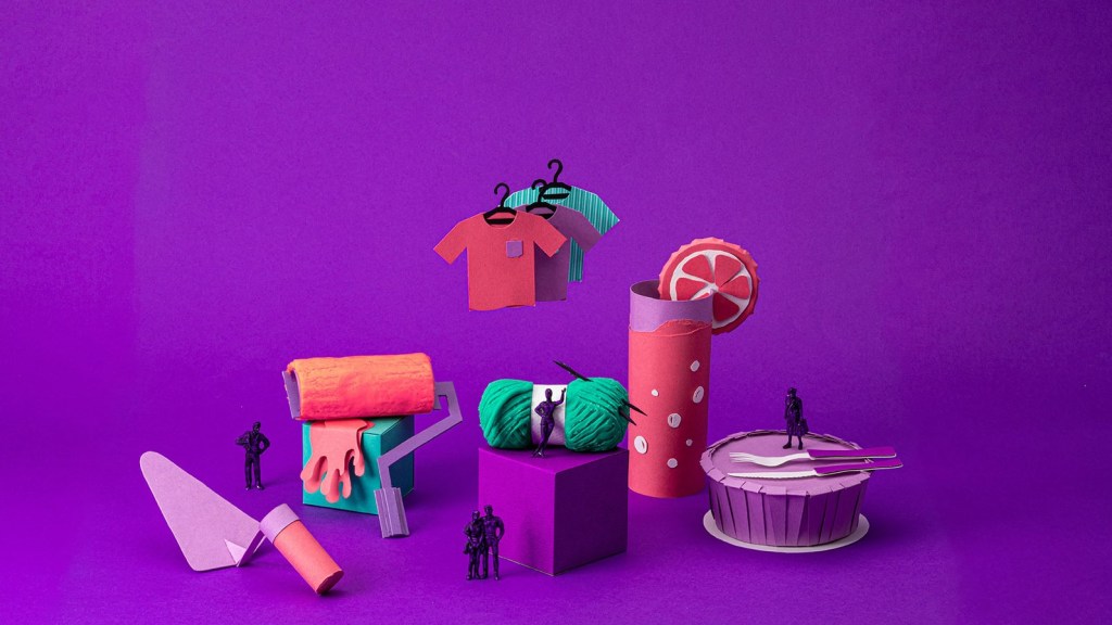 Na imagem aparecem diversos objetos de toy art sobre um fundo roxo. Pode-se ver itens relacionados à construção, como uma pá, um drink, uma marmita, duas peças de roupa, um rolo de tinta. Todos são de cores vibrantes em tons de roxo, verde e rosa.