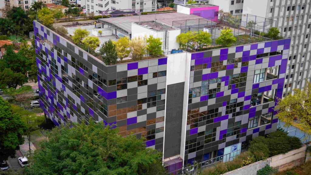 Na imagem aérea aparece o escritório do Nubank, em São Paulo, um prédio cúbico e com paredes com quadrados roxos envolto em árvores.