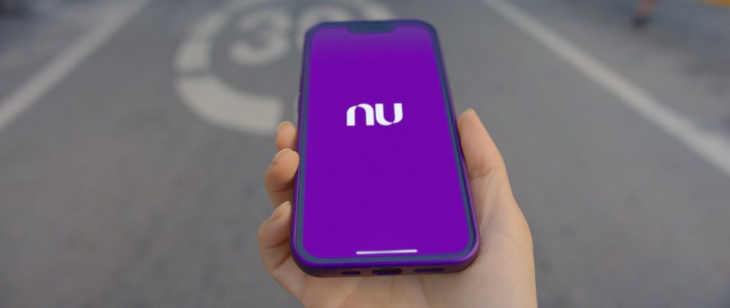 Foto mostra uma mão branca segurando um celular com o app do Nu aberto.