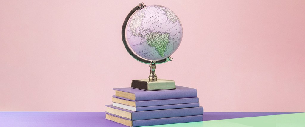 Imagem de um globo terrestre posicionado sobre uma pilha de livros com capa roxa. Ao invés de azul, as áreas do mapa que representam o mar são coloridas em um tom de lilás. O fundo da imagem é rosa claro.