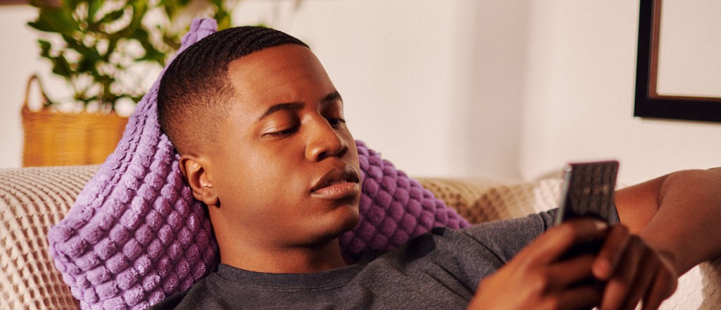 imagem de um homem negro deitado no sofá, mexendo no celular.