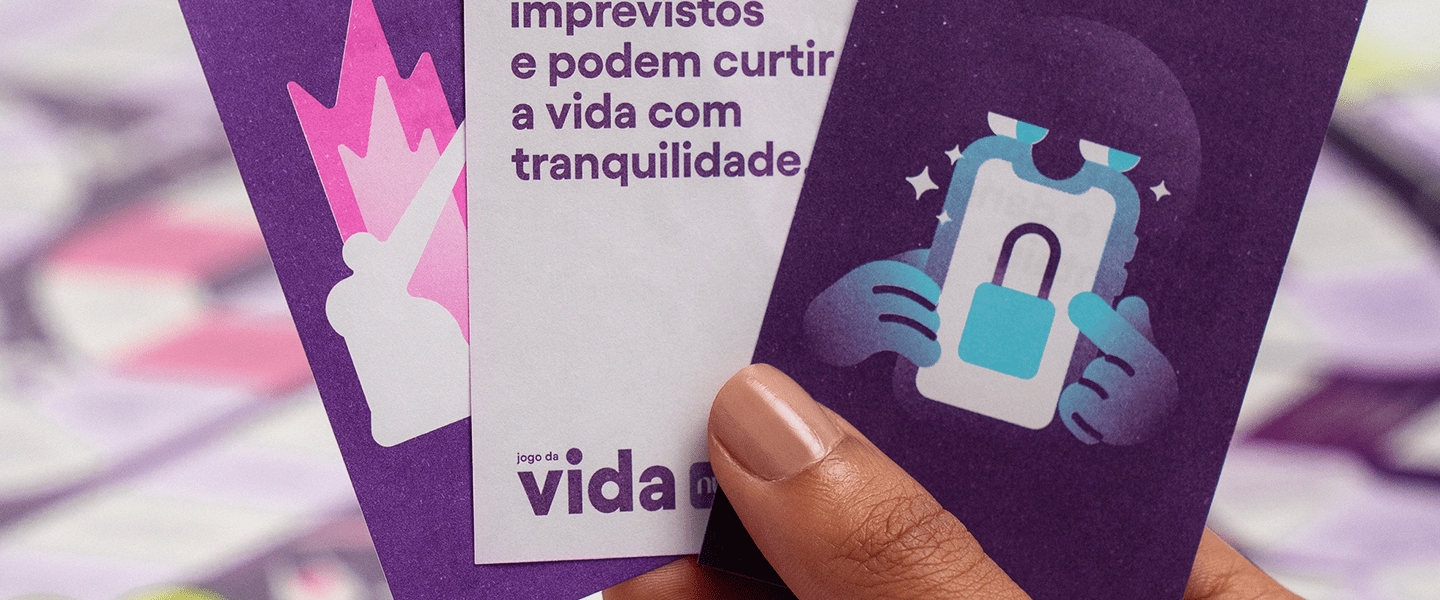 Imagem mostra uma mão segurando os cards do Jogo da Vida.