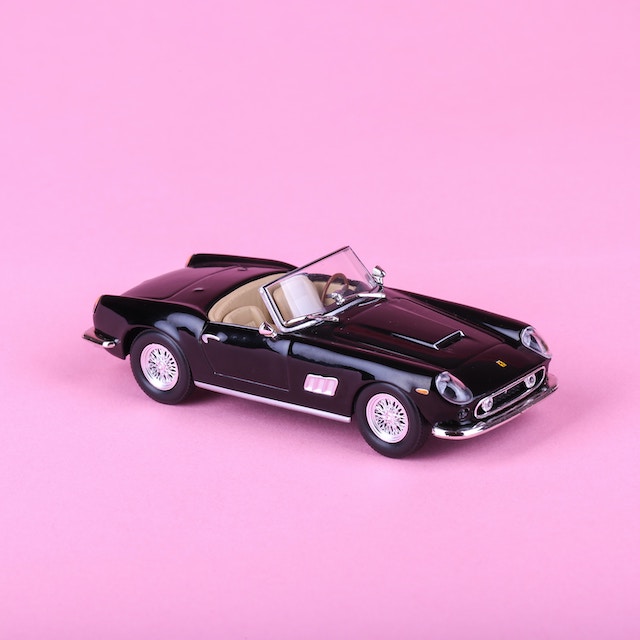 Imagem de um carro conversível preto, em miniatura, sobre uma mesa rosa claro.