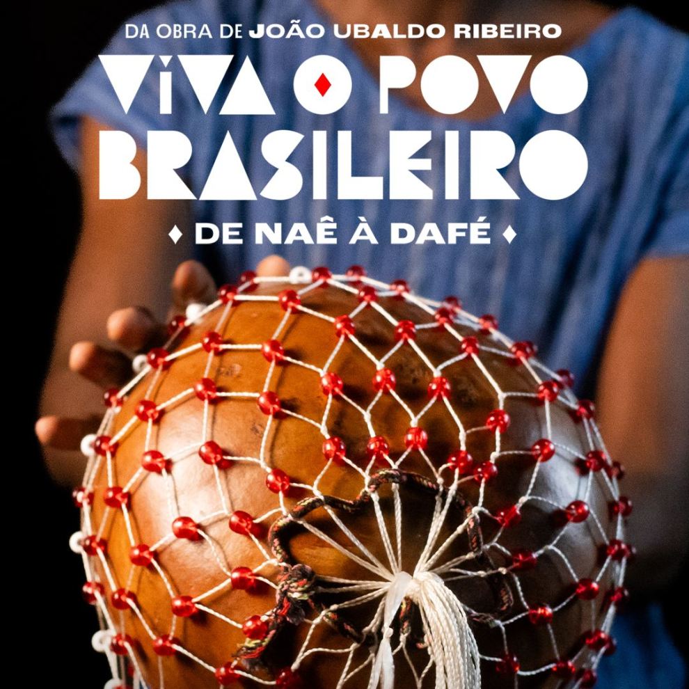 Na imagem aparece um lettering branco com o título da peça "Viva o Povo Brasileiro, de Naê a Dafé" e, ao fundo, uma imagem desfocada de uma mulher segurando um instrumento musical parecido que um xequerê