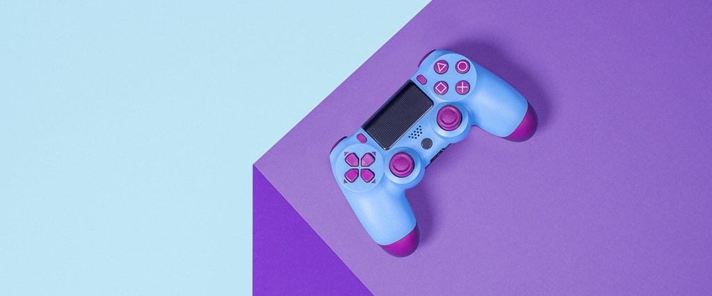Imagem mostra um controle de videogame, em tons de roxo, em cima de uma mesa, também roxa e a parece azul.