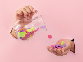 imagem de duas mãos, uma segurando uma jarra derramando moedas coloridas na outra mão. O fundo é rosa claro.