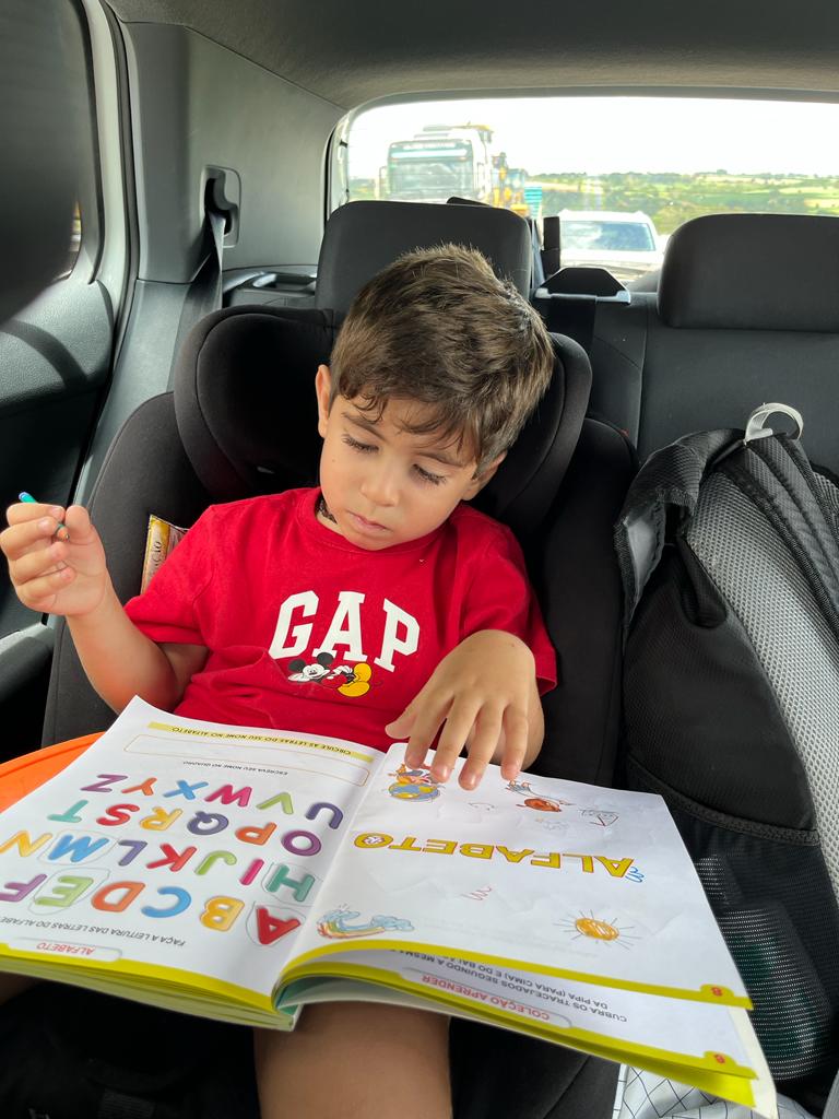 Foto de um menino com um livro de atividades no carro.