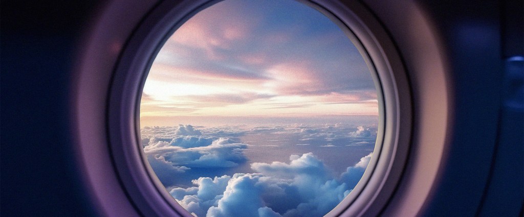 Quanto custa ir para Disney: imagem de um céu de fim de tarde, com nuvens, visto pela janela de um avião.