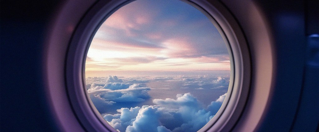 Foto da janela redonda de um avião, aparecendo as nuvens do lado de fora.