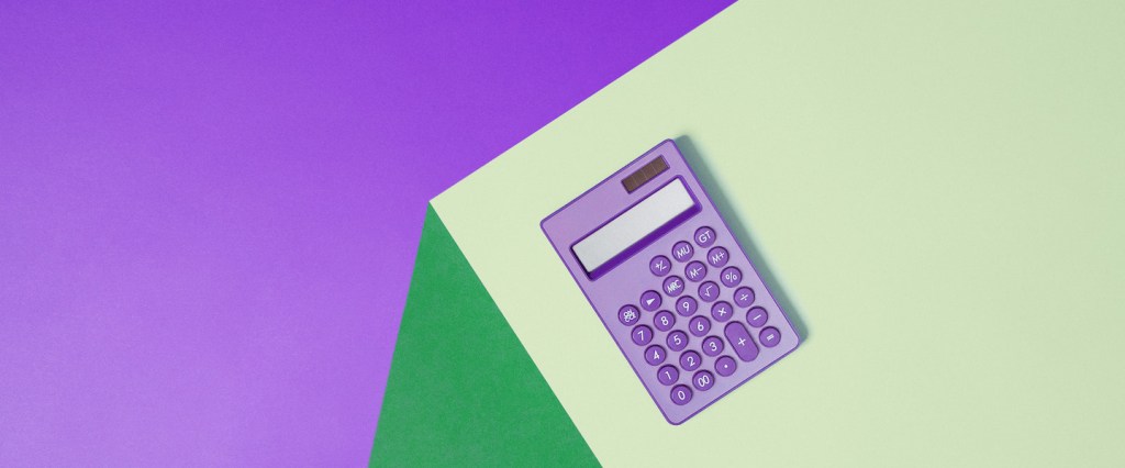 Juros rotativos: Imagem de uma calculadora roxa sobre uma mesa verde. O fundo da imagem também é roxo.
