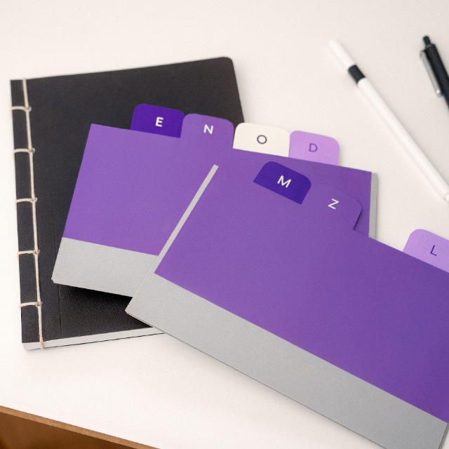 O que é MBA: Imagem de uma calculadora branca ao lado de um caderno preto e de etiquetas roxas sobre uma mesa de escritório branca.
