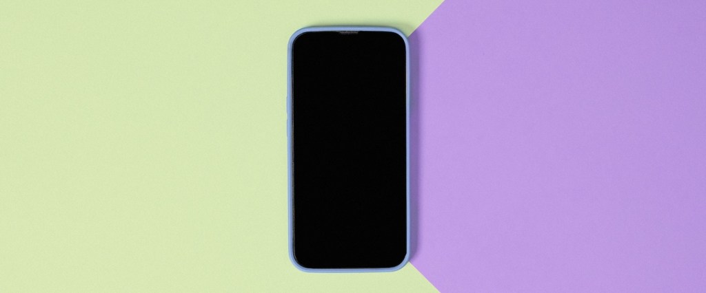 Baixar app: imagem de um celular com a tela preta no centro de uma superfície de cores verde claro e lilás.