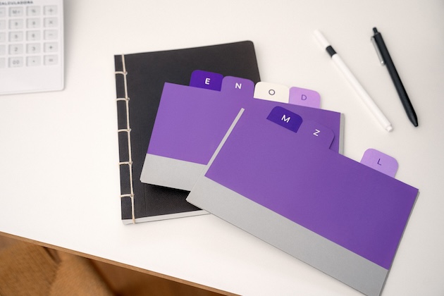 Lifelong learning: Imagem de um caderno preto e de etiquetas roxas sobre uma mesa de escritório branca.