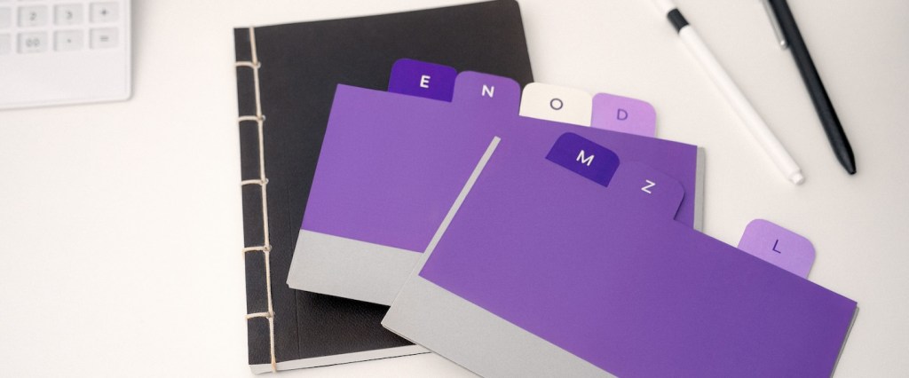 Lifelong learning: Imagem de um caderno preto e de etiquetas roxas sobre uma mesa de escritório branca.
