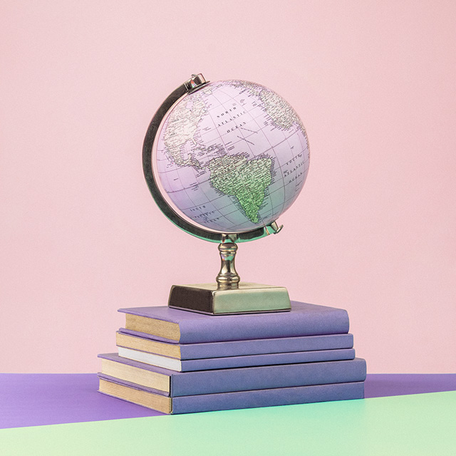 Um globo do mundo está em cima de uma pequena pilha de livros. A parede é rosa, e a mesa é roxa e verde.