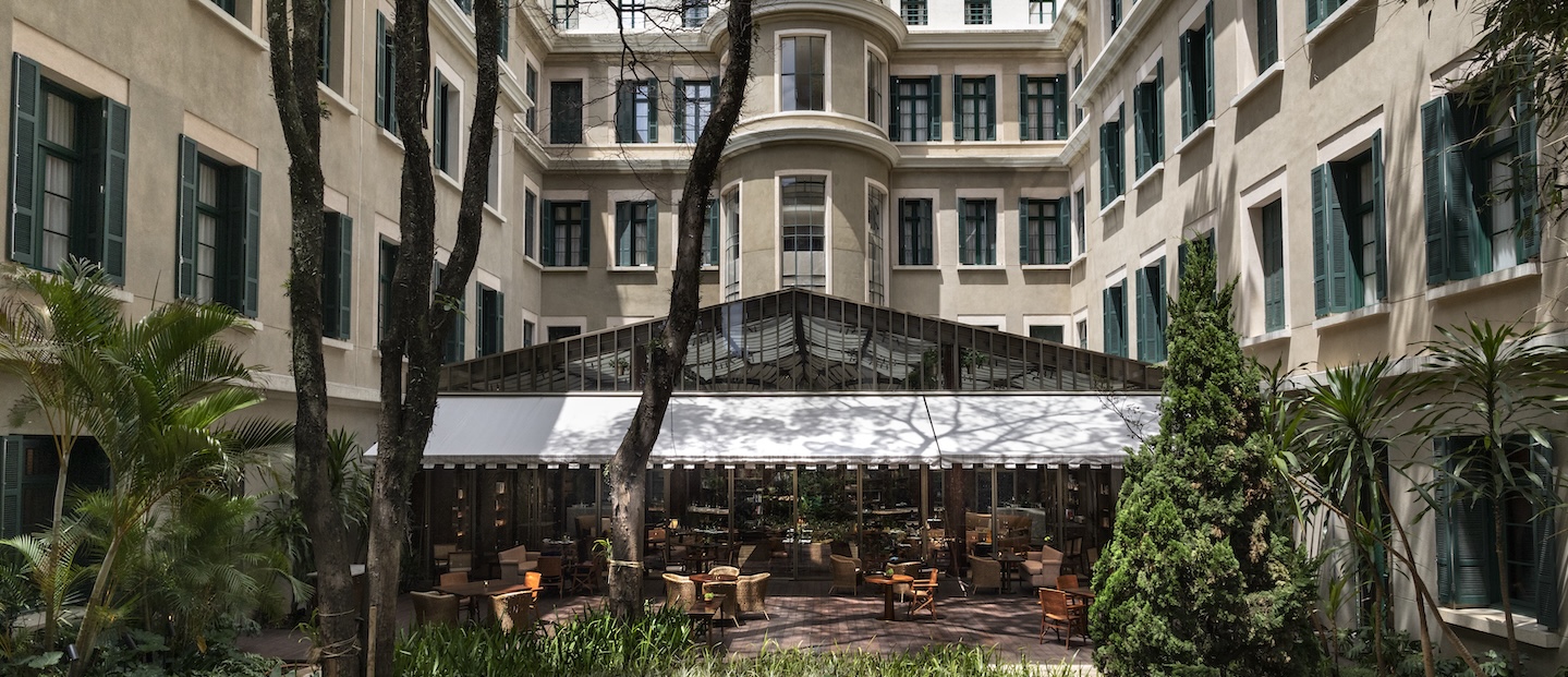 Foto da parte interna do hotel Rosewood São Paulo. O prédio é bege e rodeado por jardins.