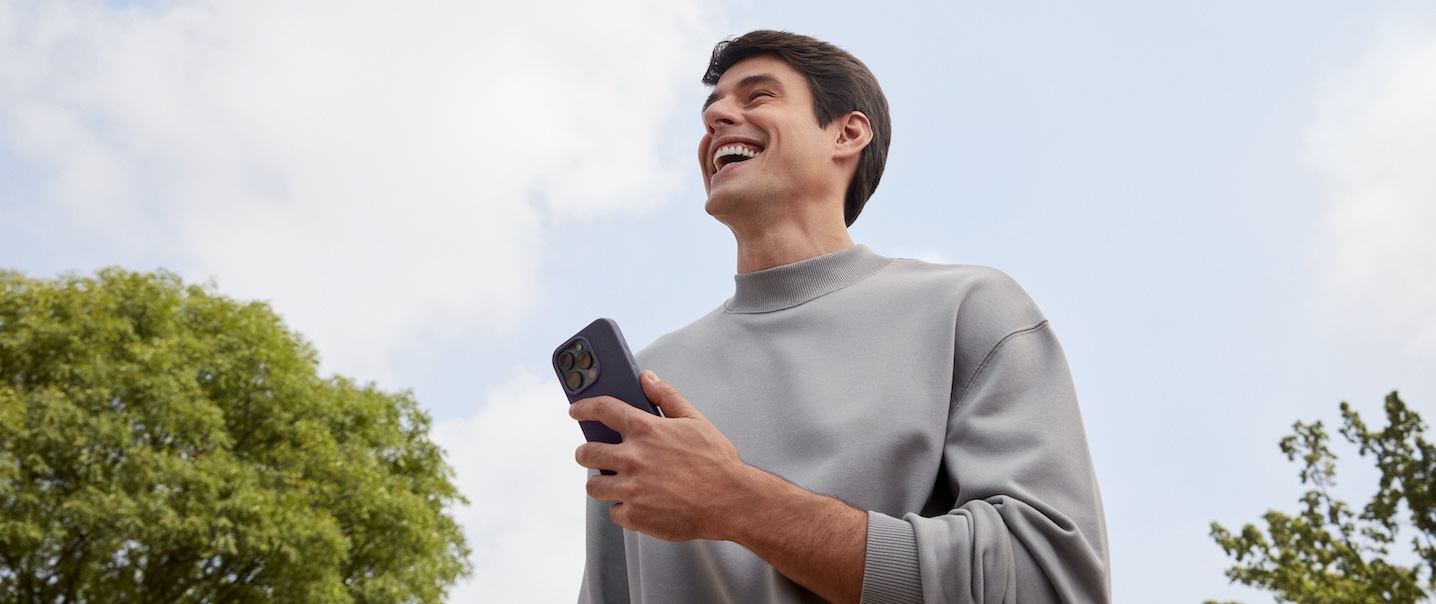 Imagem mostra homem branco, de cabelos lisos, sorrindo ao ar livre. O céu está azul. Ele veste moletom cinza.